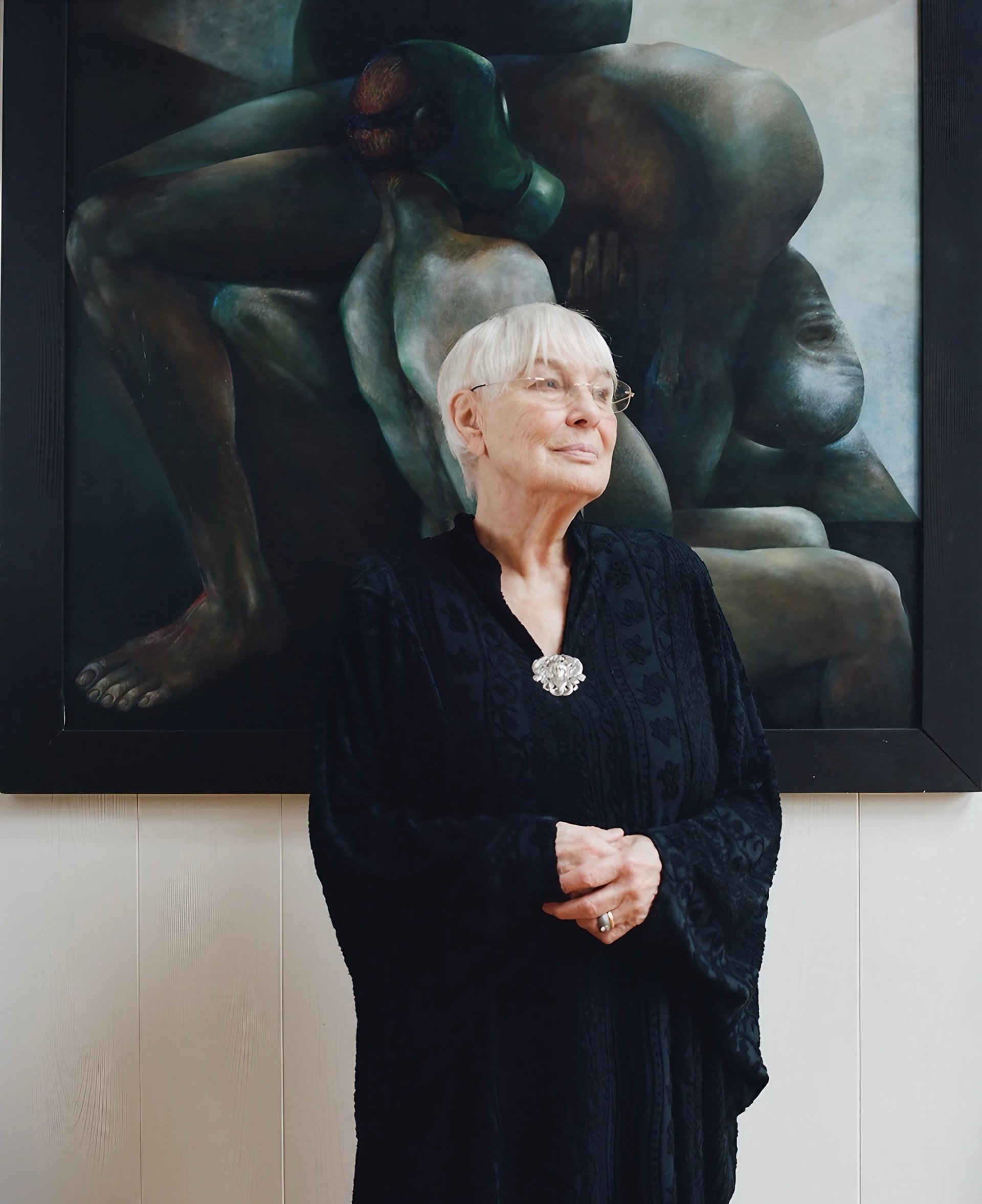 Heidrun Hegewald in schwarzem Kleid mit Brosche steht vor einem gro&szlig;formatigen Kunstwerk mit dunklen, verschlungenen K&ouml;rperformen