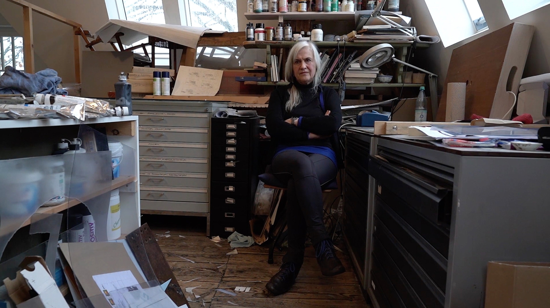 Ursula Strozynski in ihrem K&uuml;nstleratelier unter dem Dach, umgeben von Arbeitsmaterialien, Schubladenschr&auml;nken und Dachfenstern