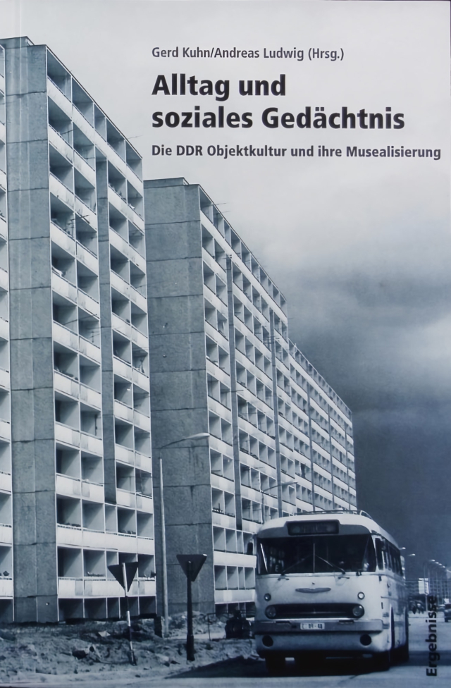 Das Buchcover ist durch drei Textebenen hierarchisch gegliedert: oben die Herausgeber "Gerd Kuhn/Andreas Ludwig (Hrsg.)", darunter in großer schwarzer Schrift der Haupttitel "Alltag und soziales Gedächtnis", gefolgt vom Untertitel "Die DDR Objektkultur und ihre Musealisierung". Diese Textelemente sind auf den oberen Bereich einer monochrom-bläulichen Fotografie gesetzt. Diese zeigt in Untersicht einen Plattenbau mit rasterartiger Balkonfront und einen davor parkenden Ikarus-Bus. Rechts unten ist dezent "Ergebnisse" platziert. Die düstere Wolkenstimmung und die strenge Architekturaufnahme visualisieren den wissenschaftlichen Charakter der Publikation.