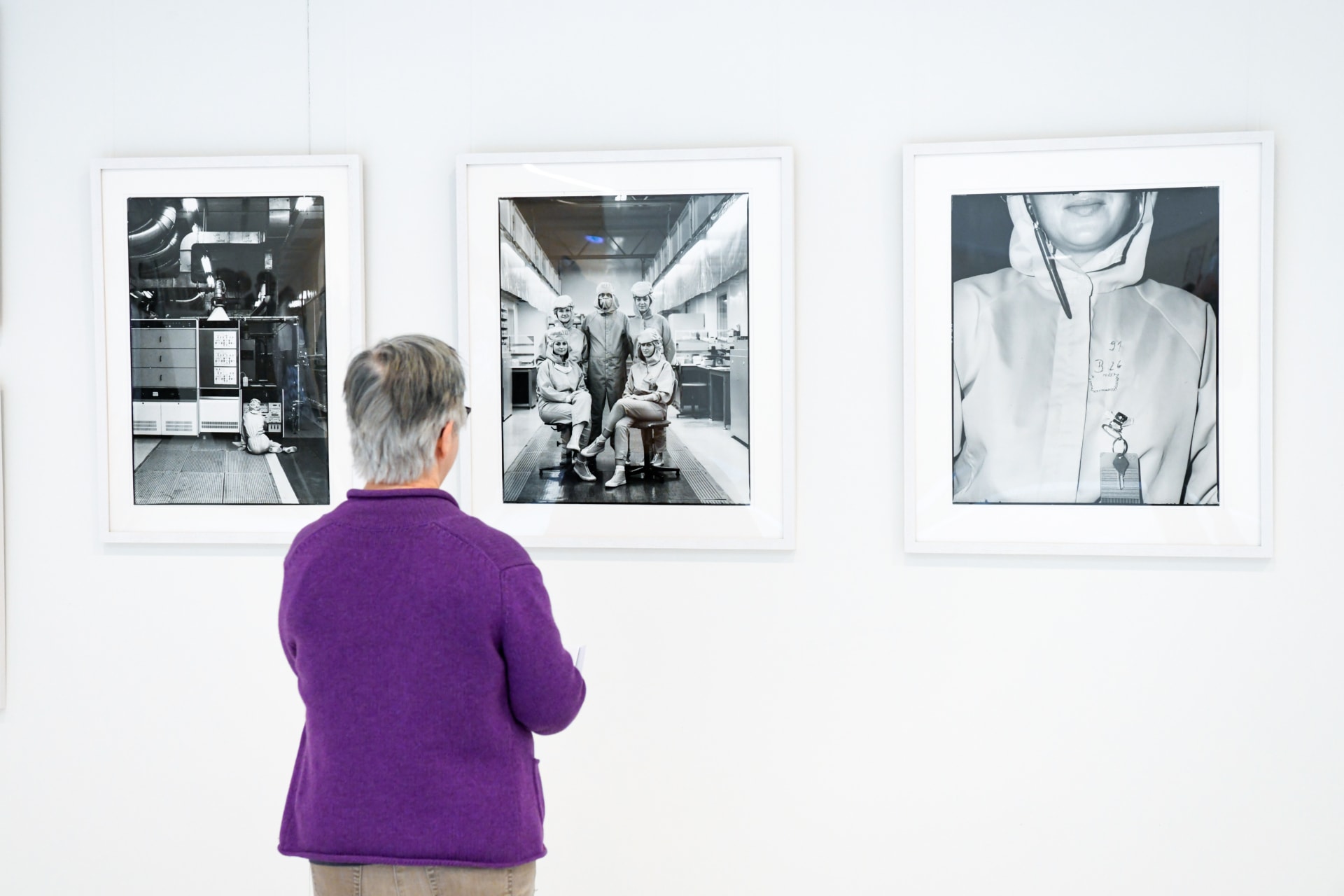 An einer wei&szlig;en Wand h&auml;ngen drei schwarz-wei&szlig;-Fotos. Davor steht eine Besucherin und schaut sich die Fotos an. Die Besucherin tr&auml;gt eine violette Strickjacke.